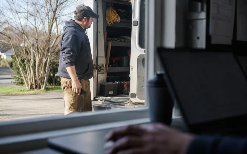Un technicien se dirigeant vers sa camionnette à l'extérieur, vu à travers un ordinateur portable posé sur un bureau à l'intérieur : la même mission, depuis le terrain et depuis le bureau.