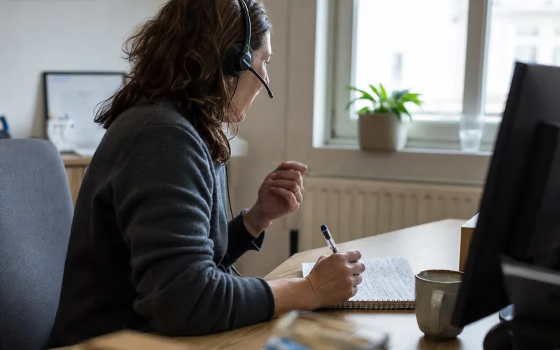 Une spécialiste du support technique, assise à son bureau, équipée d'un casque, prenant des notes pendant un appel avec un client.