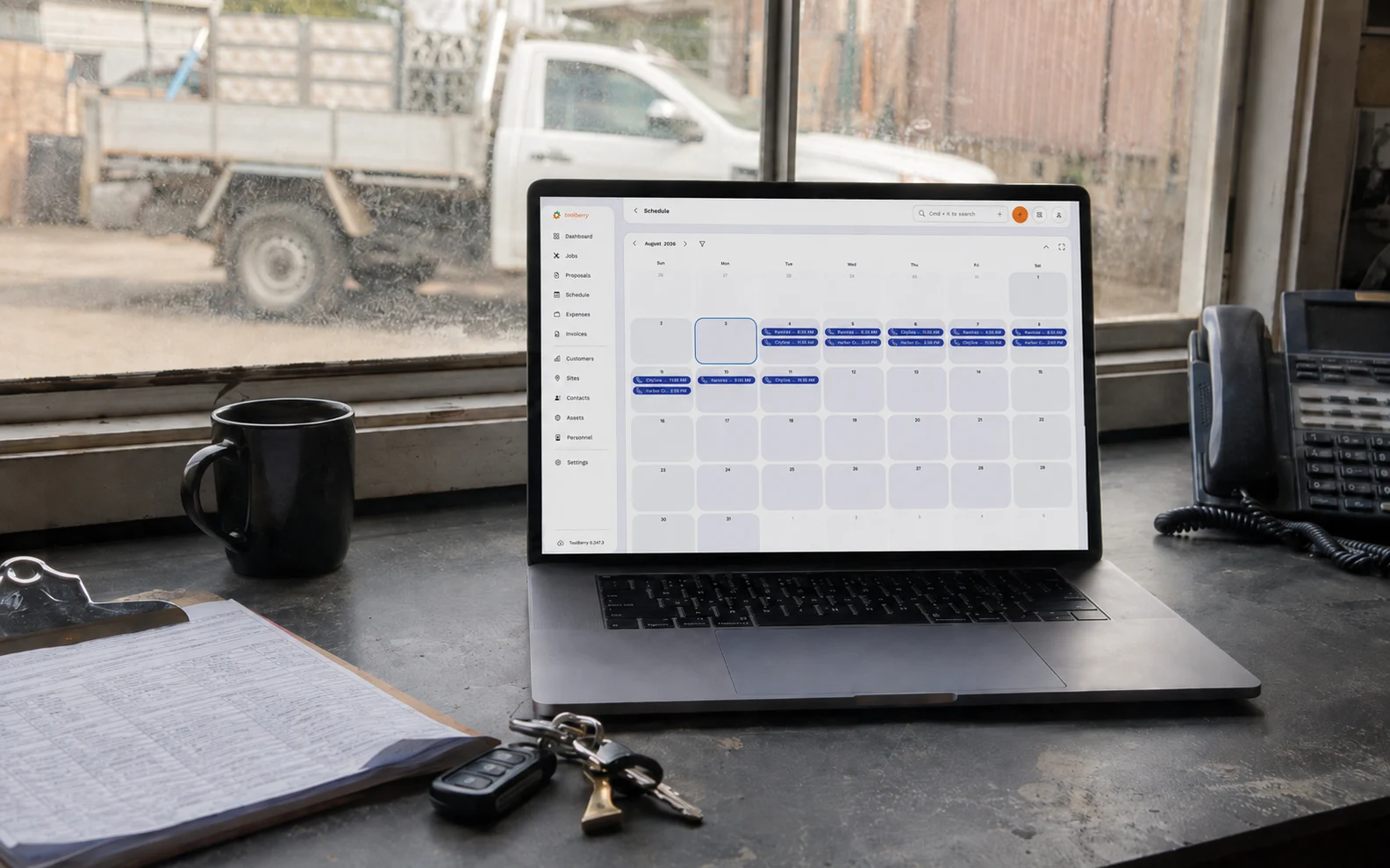 Un ordinateur portable posé sur un bureau dans un local de chantier, affichant le planning ToolBerry, avec des clés et un bloc-notes à côté.